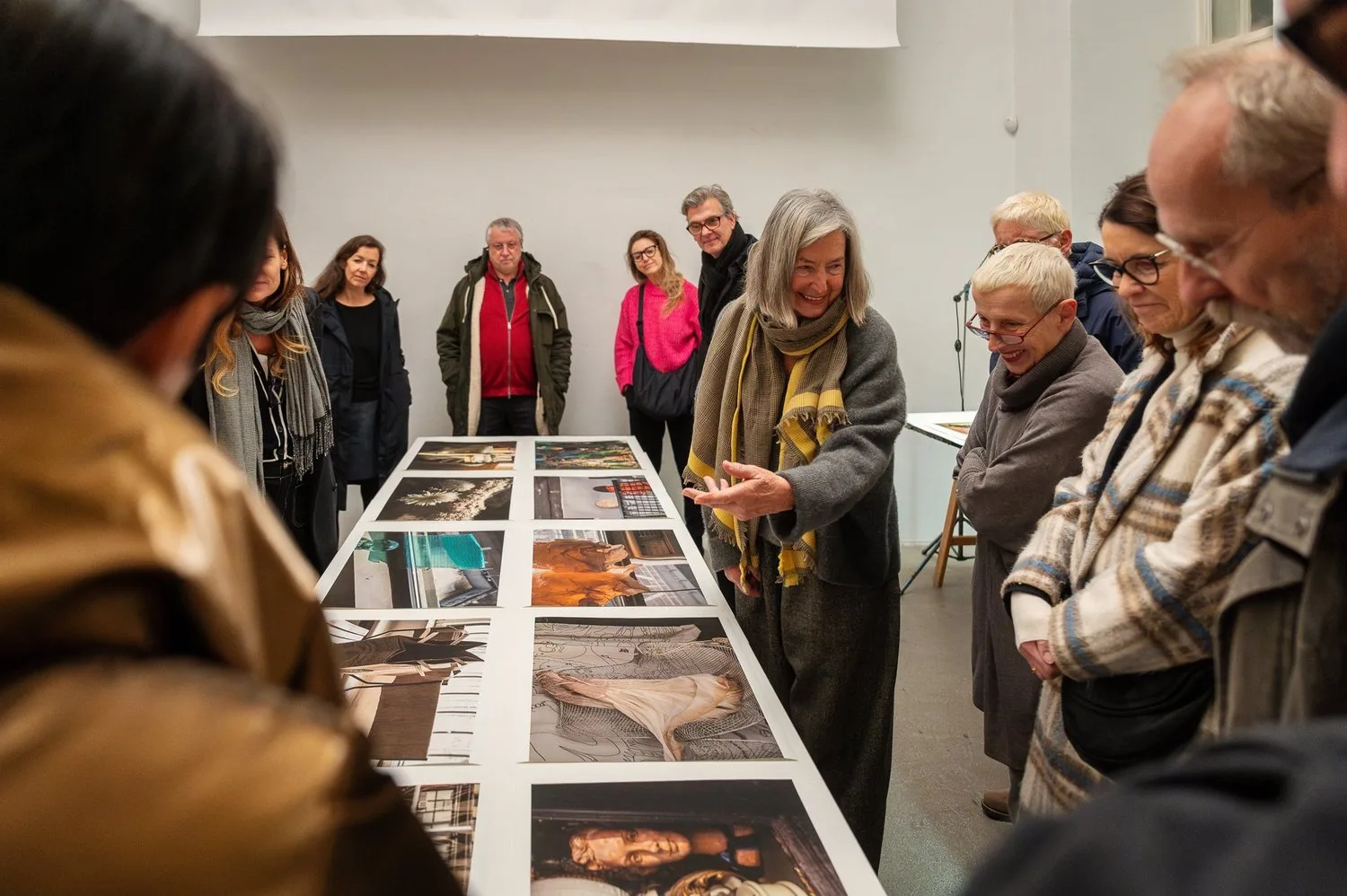 Eine Gruppe von Menschen betrachtet und diskutiert Fotos, die auf einem Tisch in einer Galerie ausgestellt sind.